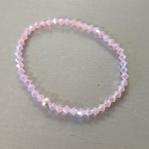 May include: A delicate pink beaded bracelet with a small silver bead. The bracelet is made of small, faceted beads that catch the light, creating a shimmering effect. The bracelet is a simple, elegant piece of jewellery.