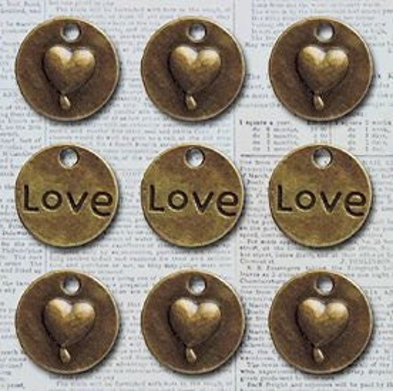 May include: Nine antique gold-toned metal charms. Three charms feature a heart design with a teardrop. Six charms feature the word "Love" in a simple font.