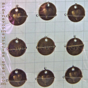 May include: Nine oval-shaped metal charms with a hole at the top. Three charms feature a heart design, three charms feature the word "Love", and three charms feature a heart design.