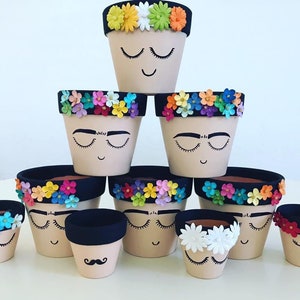 May include: A set of ten small terracotta flower pots decorated with colorful paper flowers and painted faces. The pots are arranged in a pyramid shape, with the largest pot at the top and the smallest pots at the bottom.
