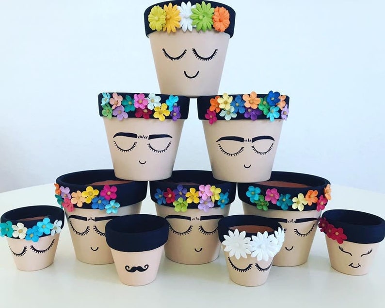 May include: A set of ten small terracotta flower pots decorated with colorful paper flowers and painted faces. The pots are arranged in a pyramid shape, with the largest pot at the top and the smallest pots at the bottom.