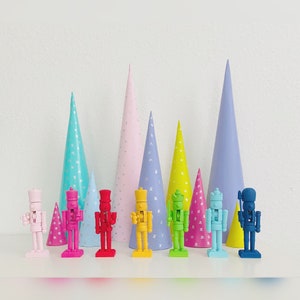 May include: A set of ten colorful nutcracker figurines standing in front of a row of pastel-colored party hats. The nutcrackers are made of painted wood and have a whimsical, festive design.