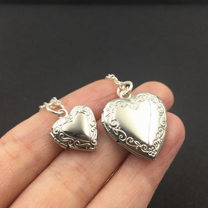 Puede incluir: Dos medallones de plata en forma de coraz&oacute;n en una cadena. El medall&oacute;n m&aacute;s grande est&aacute; en una cadena m&aacute;s larga y el medall&oacute;n m&aacute;s peque&ntilde;o est&aacute; en una cadena m&aacute;s corta.