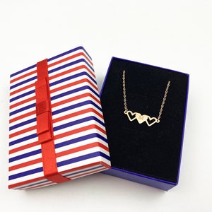 May include: A gold necklace with three connected heart charms in a blue and white striped gift box with a red ribbon.