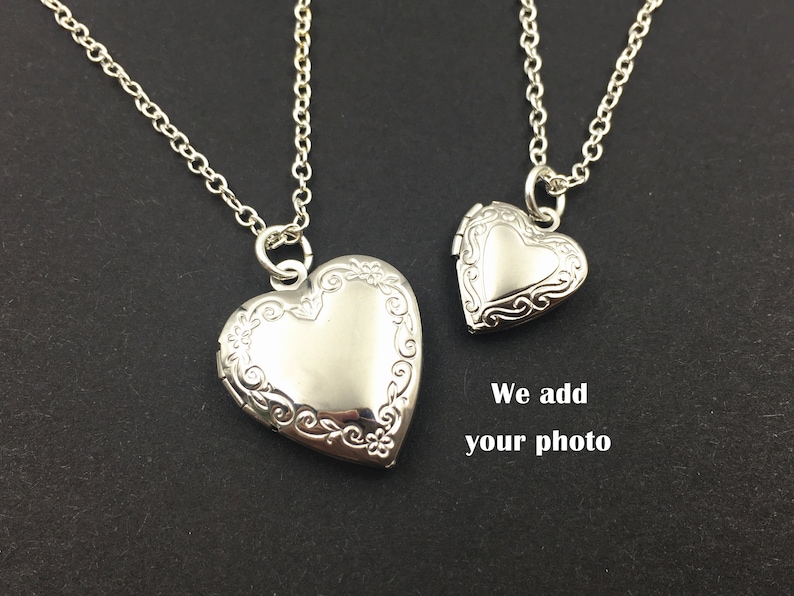 Puede incluir: Dos collares con un medall&oacute;n en forma de coraz&oacute;n plateado. El medall&oacute;n m&aacute;s grande est&aacute; en una cadena m&aacute;s larga y el medall&oacute;n m&aacute;s peque&ntilde;o est&aacute; en una cadena m&aacute;s corta.  "We add your photo" est&aacute; escrito debajo de los medallones.