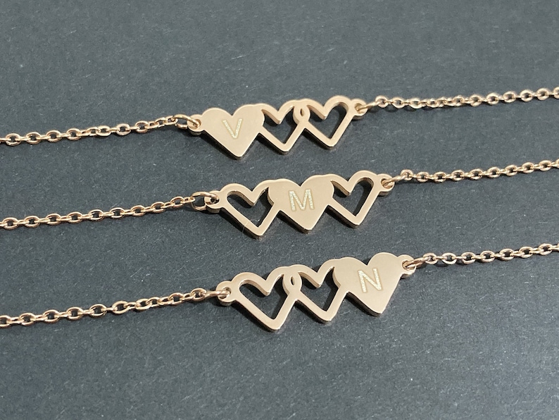 May include: Three gold-tone necklaces with heart-shaped pendants. Each pendant has a different letter engraved on it: V, M, and N.