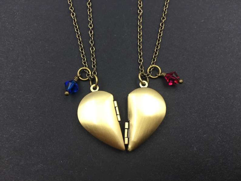 May include: Two gold heart-shaped locket necklaces with a blue and red crystal charm on each. The lockets are open and the necklaces are intertwined.