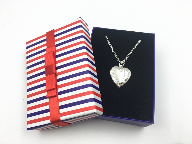 Puede incluir: Un collar con un dije en forma de coraz&oacute;n plateado en una caja de regalo a rayas azules y blancas con una cinta roja.