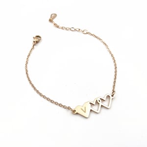 May include: Gold chain bracelet with three connected heart charms. The center heart charm has a small letter 'V' engraved inside.