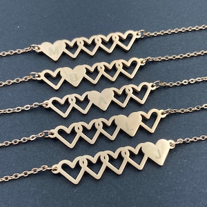 May include: Five gold necklaces with interlocking heart pendants. Each heart has a different letter engraved on it: M, B, A, L, and J.