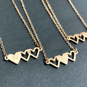 May include: Three gold necklaces with three interlocking heart charms. Each heart has a different initial engraved on it: N, M, and S.