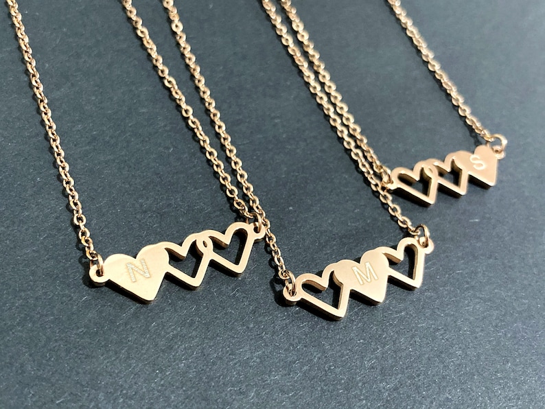 May include: Three gold necklaces with three interlocking heart charms. Each heart has a different initial engraved on it: N, M, and S.