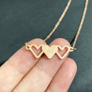 May include: Gold necklace with three interlocking heart charms. The middle heart charm has the letter "M" engraved inside.