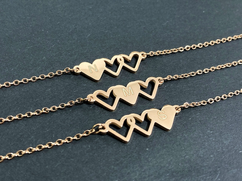 May include: Three gold-tone necklaces with interlocking heart pendants. Each heart has a different initial engraved on it: N, M, and S.