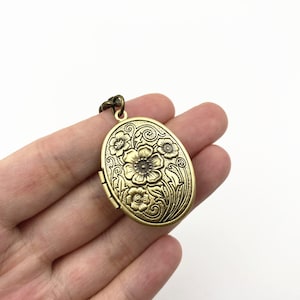 Puede incluir: Un collar con un medall&oacute;n ovalado de color dorado, adornado con un dise&ntilde;o floral. El medall&oacute;n est&aacute; grabado con flores y hojas.