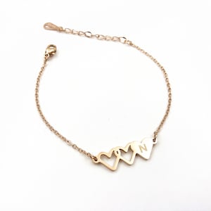 May include: A gold chain bracelet with three interlocking heart charms. The charm on the right has the letter "N" engraved on it.