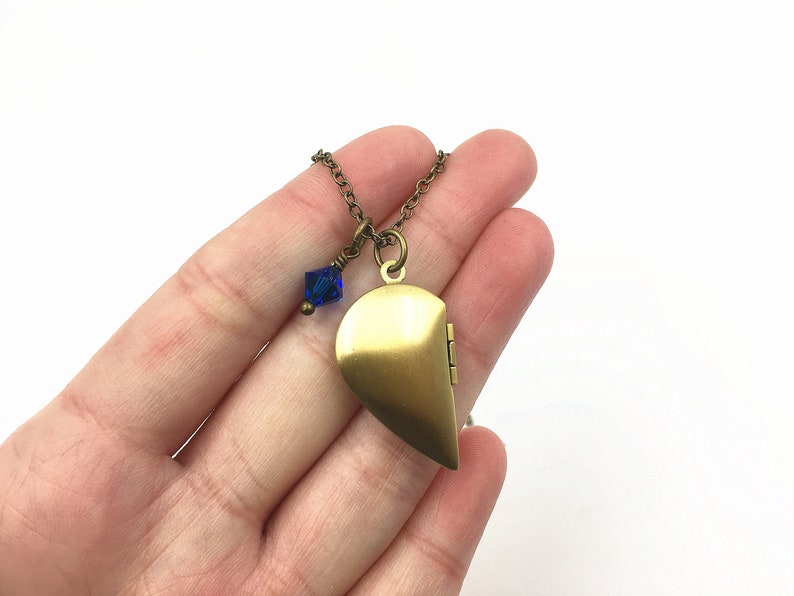 May include: A gold-toned heart-shaped locket necklace with a blue crystal charm. The locket opens to reveal a small compartment for holding a photo or other small items.