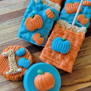 May include: An assortment of festive treats, including rectangular rice crispy treats dipped in orange and blue candy melts, decorated with orange and blue pumpkin candies. A round treat with the number 1 and a blue candy with an orange pumpkin are also present.
