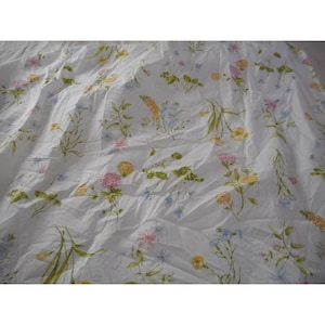May include: White fabric with a floral pattern featuring pink, yellow, and blue flowers, along with green leaves and stems. The fabric is wrinkled, suggesting it may be a sheet or tablecloth.