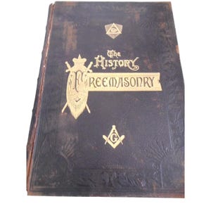 Puede incluir: Libro antiguo titulado "The History of Freemasonry" con letras y símbolos dorados sobre una cubierta azul oscuro. La cubierta presenta patrones florales en relieve y emblemas masónicos.