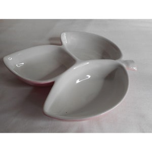 May include: A white ceramic serving dish shaped like three leaves with pink rims. The dish is ideal for serving snacks or appetizers.
