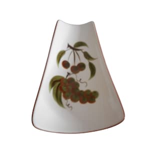 May include: White ceramic spoon rest with a cherry design. The spoon rest is triangular with a curved top. The cherry design features red cherries and green leaves. The edges of the spoon rest are brown.