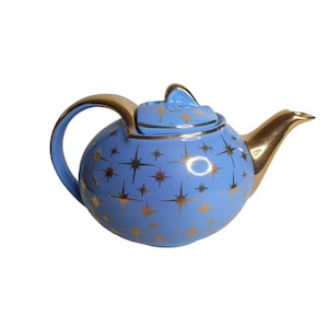 Może przedstawiać: Niebieski czajnik z motywem złotych gwiazd. Czajnik ma pokrywkę i dzióbek.