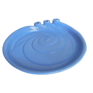 Puede incluir: Un plato de cerámica azul claro con un diseño en espiral. El plato tiene tres pequeñas hendiduras en un lado, posiblemente para velas.
