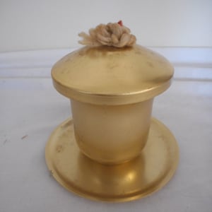 May include: A gold metal candle holder with a round top and a wick. The candle holder is on a gold metal base.