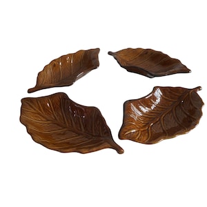May include: Set of four brown ceramic leaf-shaped serving dishes. The dishes are glazed and have a raised leaf design.