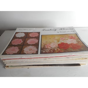 May include: A stack of paper painting instruction books with a cover featuring a painting of pink and red flowers with green leaves. The title of the book is "Fantasy Flowers by Georgie Bartlett".