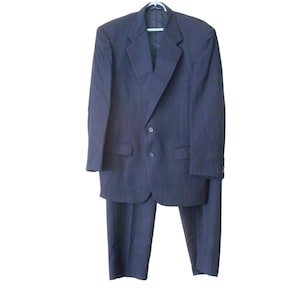 May include: A navy blue suit, including a blazer and trousers, hangs on a white hanger. The blazer has a two-button closure and notched lapels. The suit appears to be made of a textured fabric.