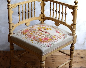 May include: Antique corner chair with a light yellow painted wooden frame. The chair features a detailed backrest with vertical spindles and a floral tapestry seat cushion. The chair's legs are connected by horizontal supports, and the overall design is ornate.
