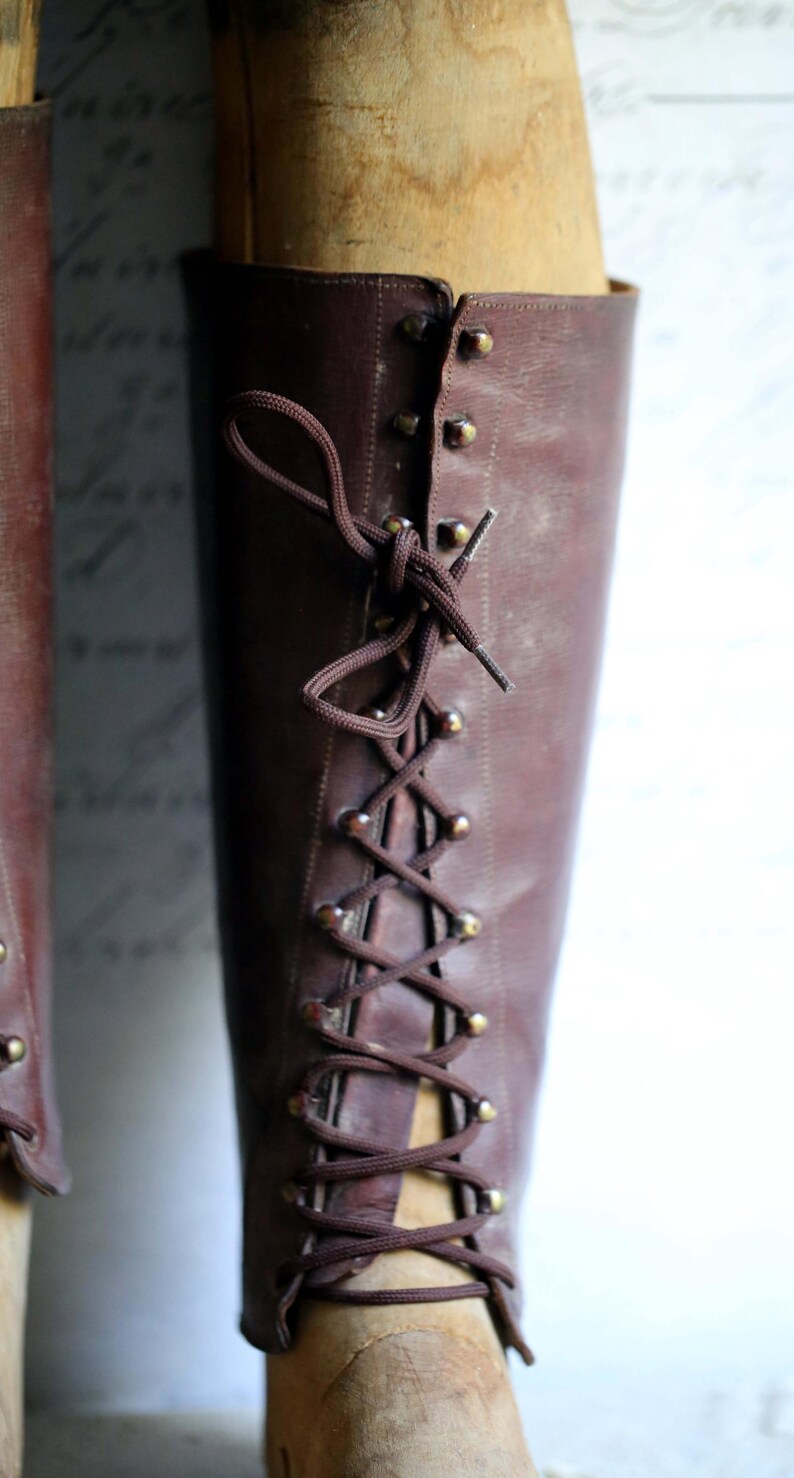 May include: A close-up of a brown leather boot with a lace-up design. The boot has a vintage look, with brass-colored eyelets and a dark brown lace. The boot is displayed on a wooden form.