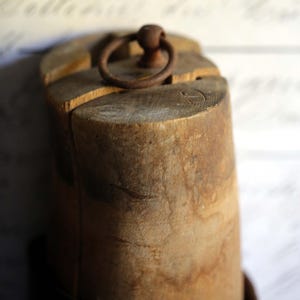 May include: A weathered wooden object with a circular metal ring on top. The wood has a natural, aged appearance with visible grain and texture. The ring is a rusty brown color, adding to the vintage aesthetic. The object appears to be a decorative or functional item.
