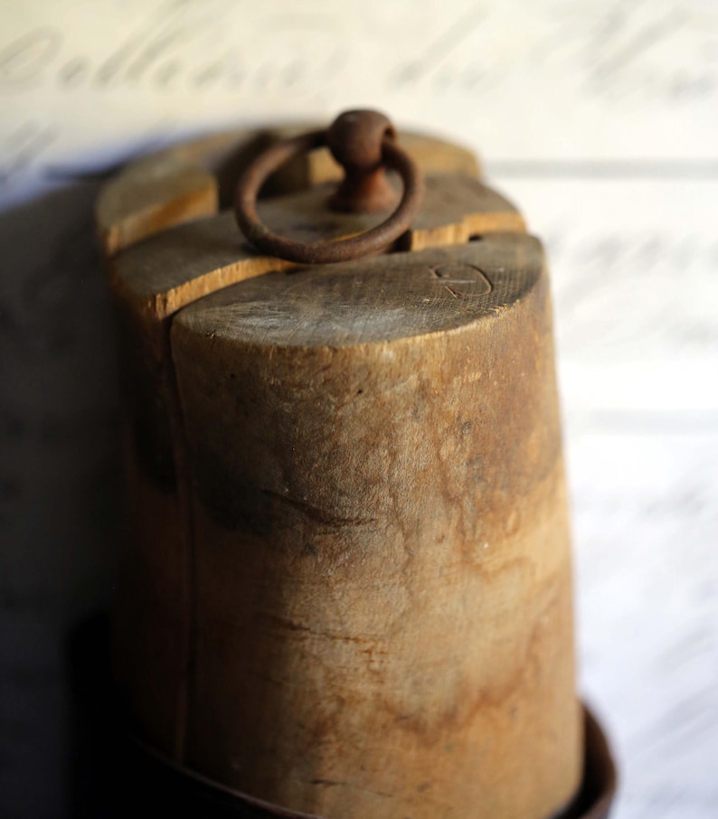 May include: A weathered wooden object with a circular metal ring on top. The wood has a natural, aged appearance with visible grain and texture. The ring is a rusty brown color, adding to the vintage aesthetic. The object appears to be a decorative or functional item.