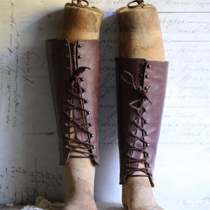 May include: Two vintage brown leather boots, each with a wooden form inside. The boots are knee-high, featuring a lace-up design. They are set against a backdrop of aged paper with handwritten script.