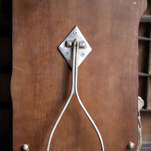 May include: A wooden picture frame with a silver metal stand. The stand is attached to the back of the frame with screws. The frame has a decorative design on the edges.