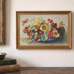 May include: A framed oil painting depicting a cluster of vibrant red, orange, and yellow nasturtium flowers arranged in a dark blue bowl. The artwork features visible brushstrokes and is signed and dated in the lower right corner as A. Le Witt 22.5.58.