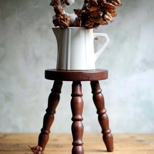 May include: A white ceramic mug with a black handle and the text "But First, Coffee" in a black, bold font. The mug is on a white surface.