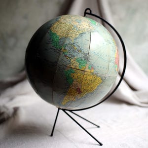 以下が含まれることがあります： 黒い金属製のスタンドに取り付けられた、詳細な世界地図が描かれたヴィンテージ地球儀。 地球儀は、国や大陸を表すさまざまな色を使用したクラシックなデザインです。 スタンドは三脚ベースと湾曲したサポートを備えています。