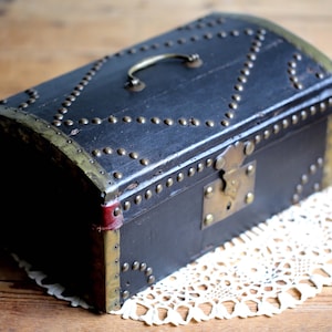 May include: A black wooden box with brass accents and a metal latch. The box is decorated with metal studs and has a curved top.