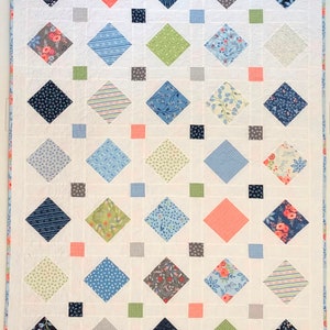 A quilt with a white background and a diamond pattern. The diamonds are in various colors and patterns, including blue, green, gray, pink, and floral. The quilt is edged with a light blue trim.