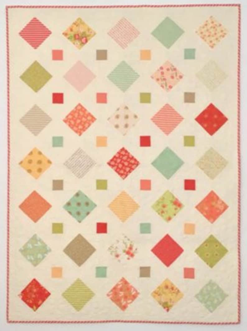A quilt with a white background and a diamond pattern. The diamonds are in various colors, including red, pink, green, brown, and yellow. The quilt is edged with a red and white trim.