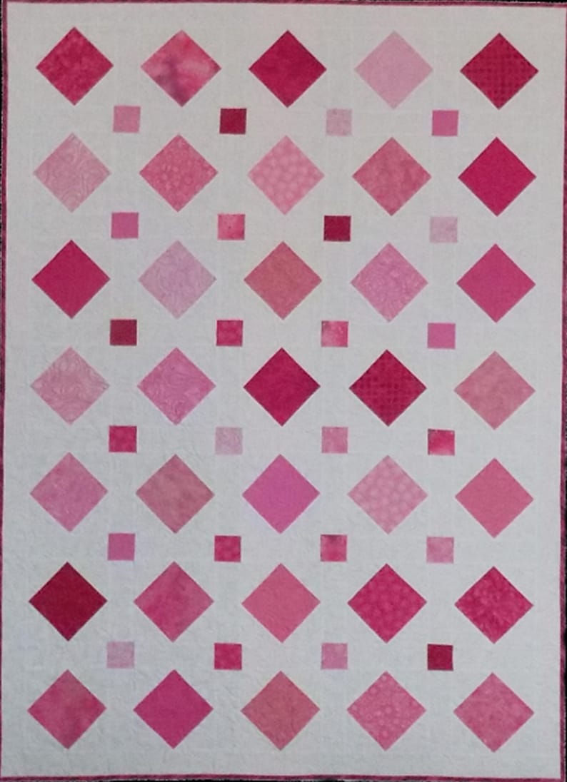 A quilt with a white background features a grid of alternating pink diamond and square patches. The vibrant pink tones create a harmonious pattern.