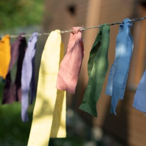 May include: A line of colorful fabric strips hanging on a clothesline. The strips are in shades of yellow, green, blue, brown, pink, and purple.