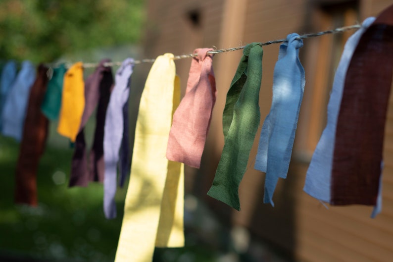 May include: A line of colorful fabric strips hanging on a clothesline. The strips are in shades of yellow, green, blue, brown, pink, and purple.
