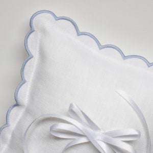 May include: White ring pillow with a blue scalloped edge and a white satin ribbon tied in a bow.