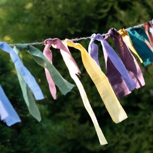 May include: A string of colorful fabric bunting, with each flag tied in a knot. The bunting is made of different shades of blue, green, yellow, purple, and pink.