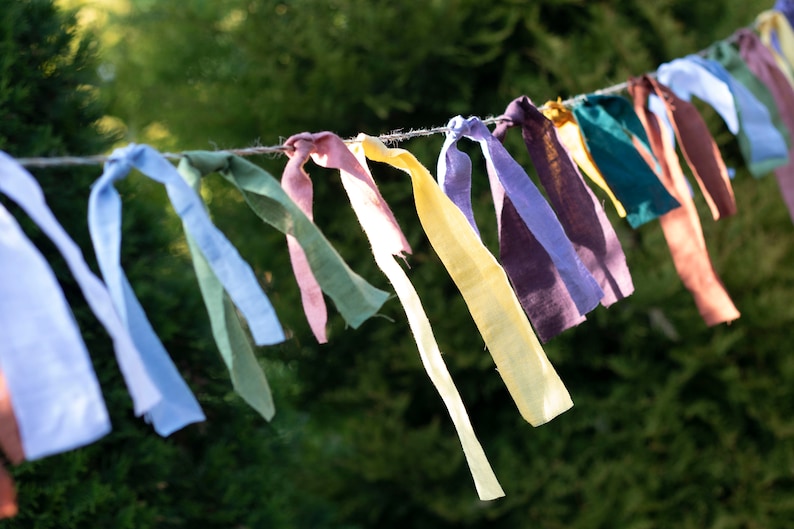 May include: A string of colorful fabric bunting, with each flag tied in a knot. The bunting is made of different shades of blue, green, yellow, purple, and pink.